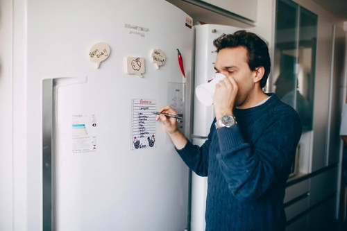 Man writing notes on fridge door