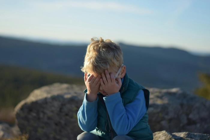Upset little boy covering his face outdoors