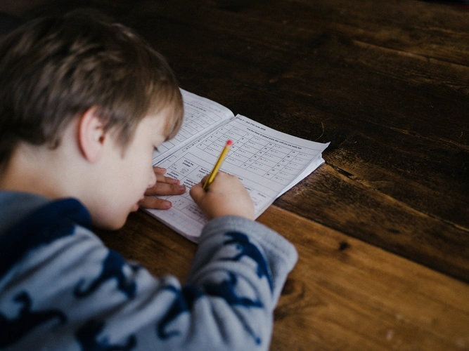 Boy doing homework with a pencil at wooden table