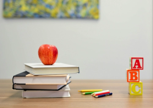 Stack of books with an apple, colored pencils, and alphabet blocks