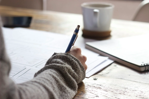 Hand writing on sketches with a blue pen on a wooden desk