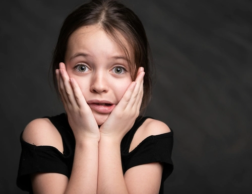 A little girl with a scared expression, hands on her cheeks