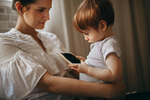 Mother holding toddler who uses a smartphone