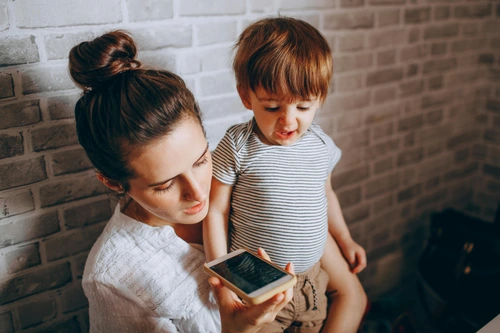 Woman with upset toddler looking at mobile phone