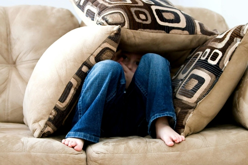 Child hiding under pillows on the sofa