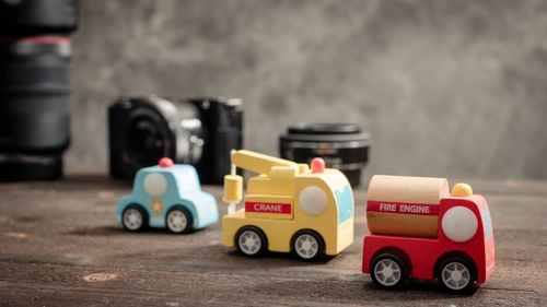 Wooden toy vehicles including police car, crane and fire engine with cameras in the background