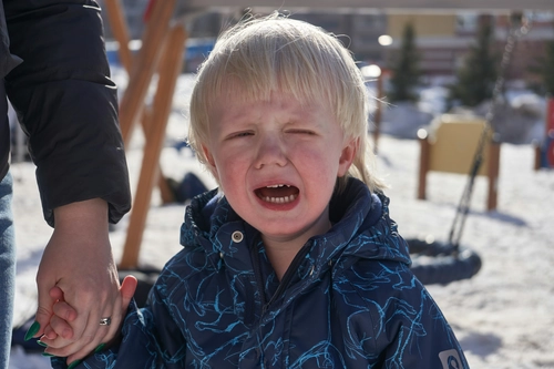 Little boy crying while holding an adult's hand in a snowy playground.